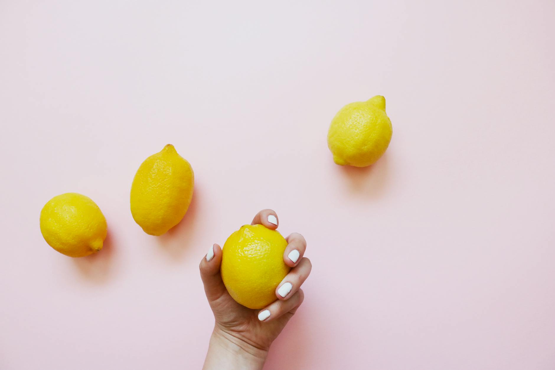 A hand holding a fresh lemon on a soft pink background, symbolizing the gentle yet stimulating nature of lemon vibrator sensation.