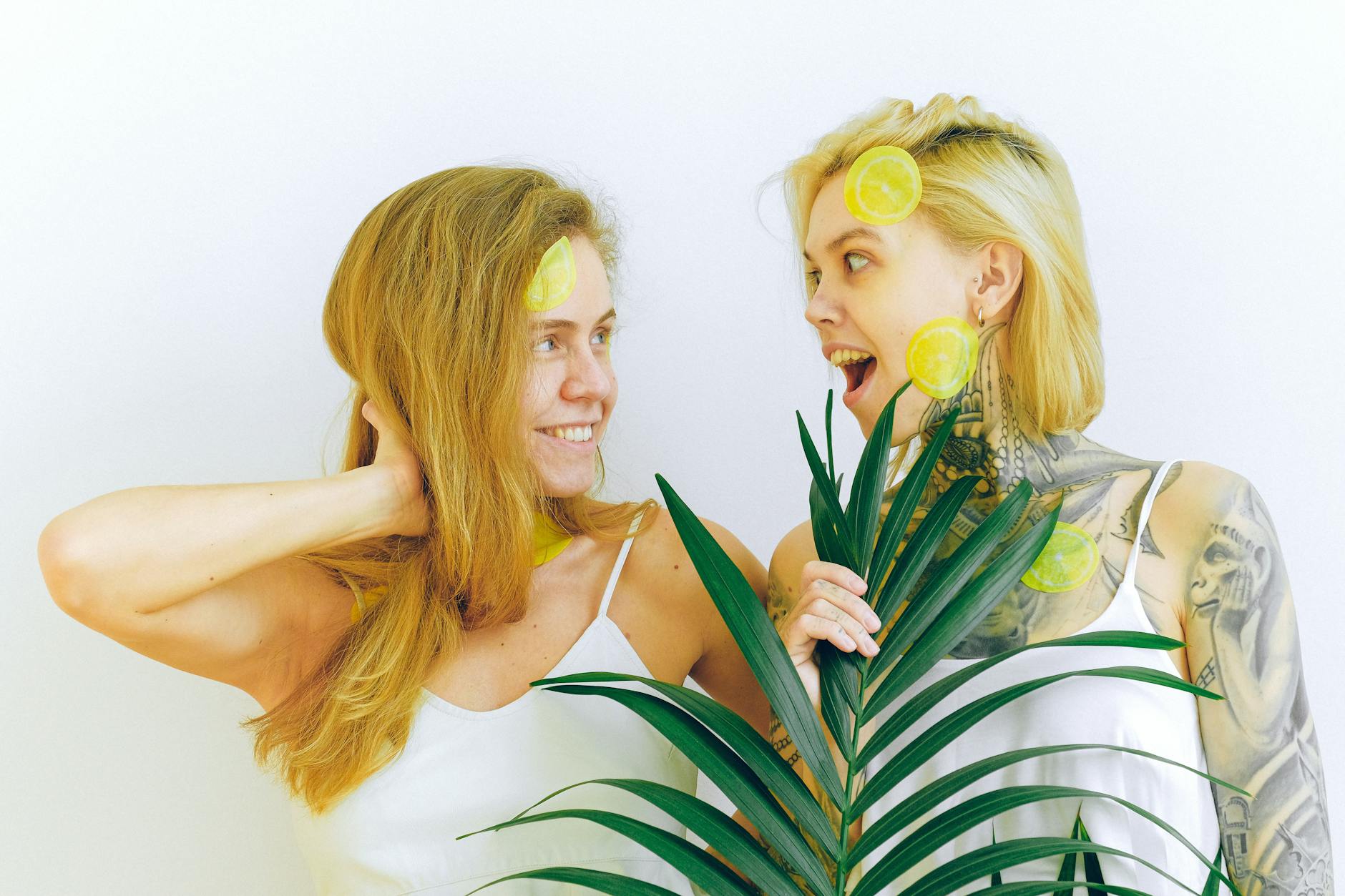 Two women smiling joyfully while holding lemon slices indoors