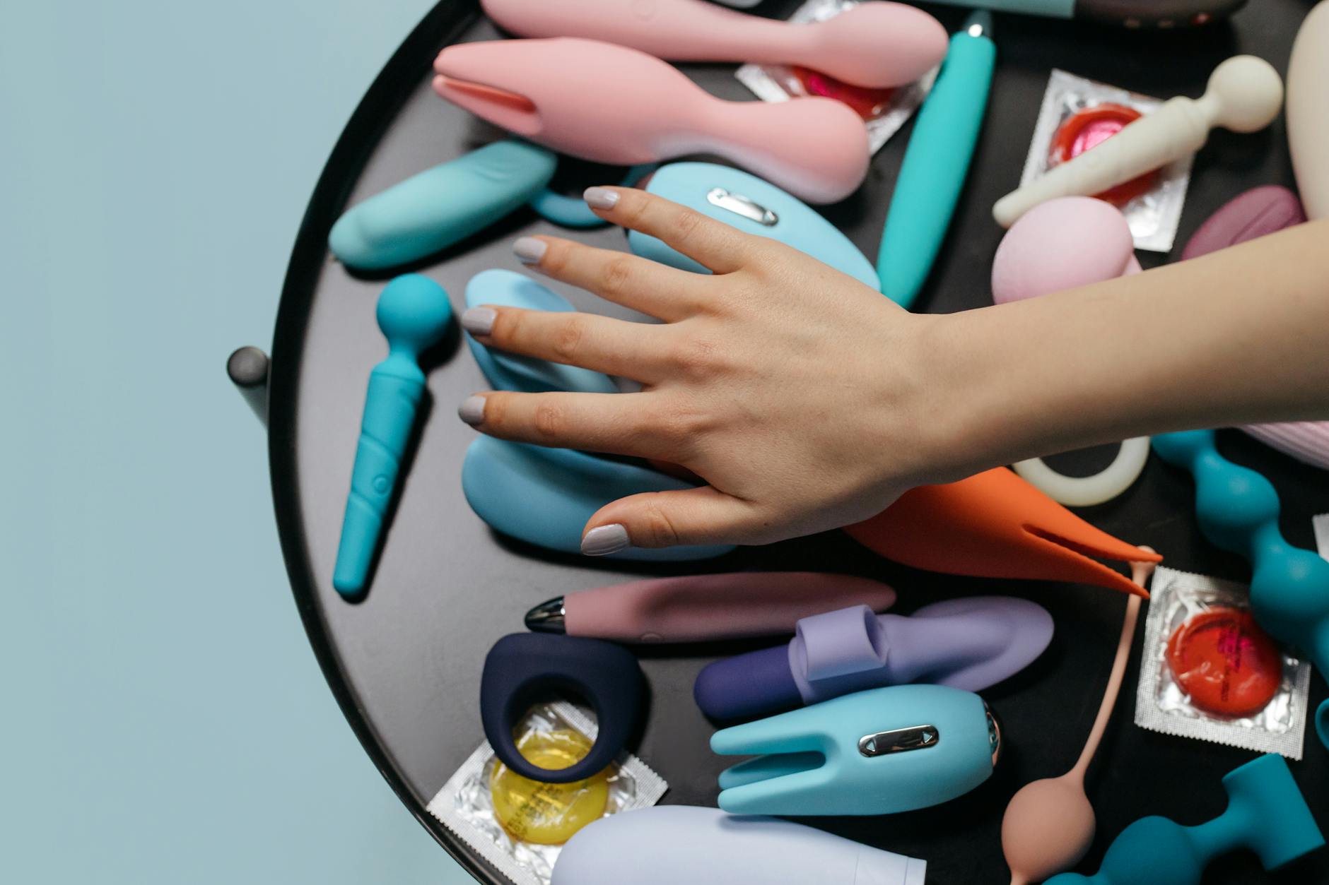 A hand reaching over a variety of colorful lemon clitoral vibrators arranged on a table.