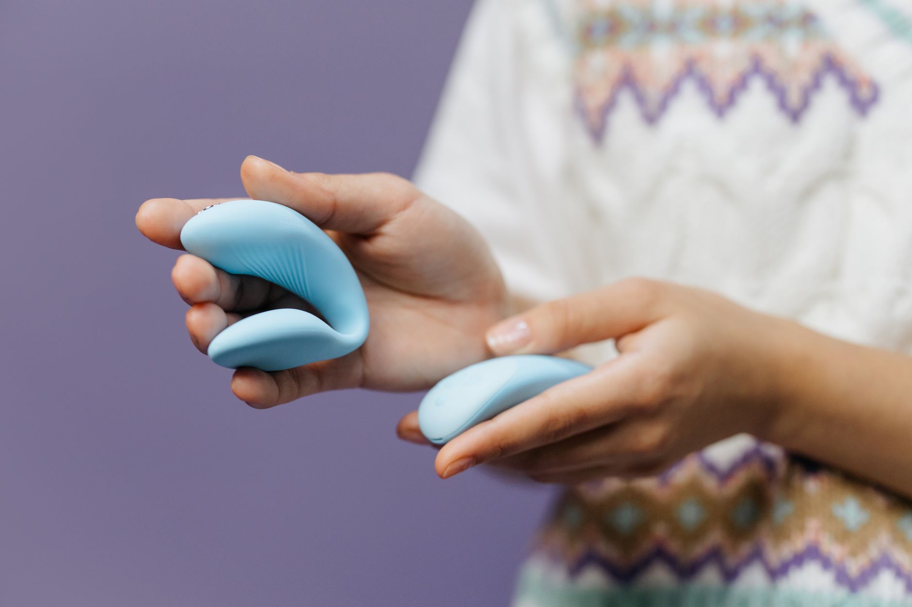 Hands holding a sleek blue lemon vibrator, intimate and calm against a purple background.