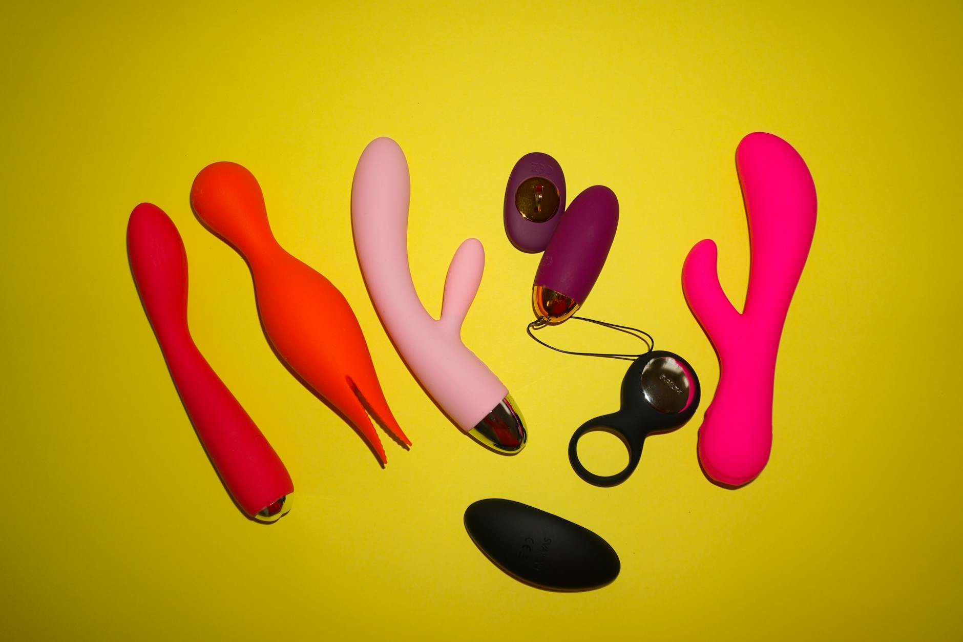 Colorful sex toys arranged on a bright yellow background, including various clitoral vibrators and toys